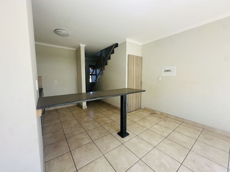 An open-plan living area featuring tiled flooring, a breakfast bar, and a staircase leading to the upper level.