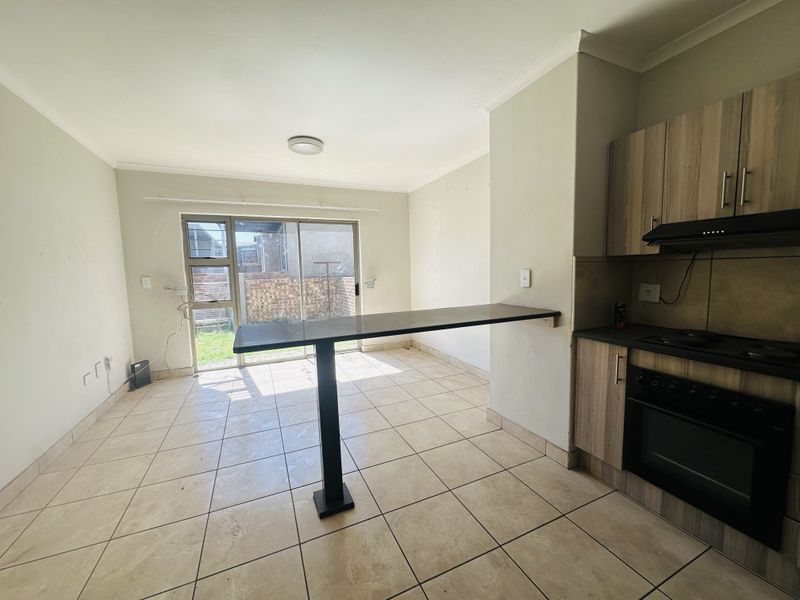 Open-plan kitchen and living area featuring tiled floors, built-in cabinetry with oven and extractor, and a breakfast bar leading to a sliding door.