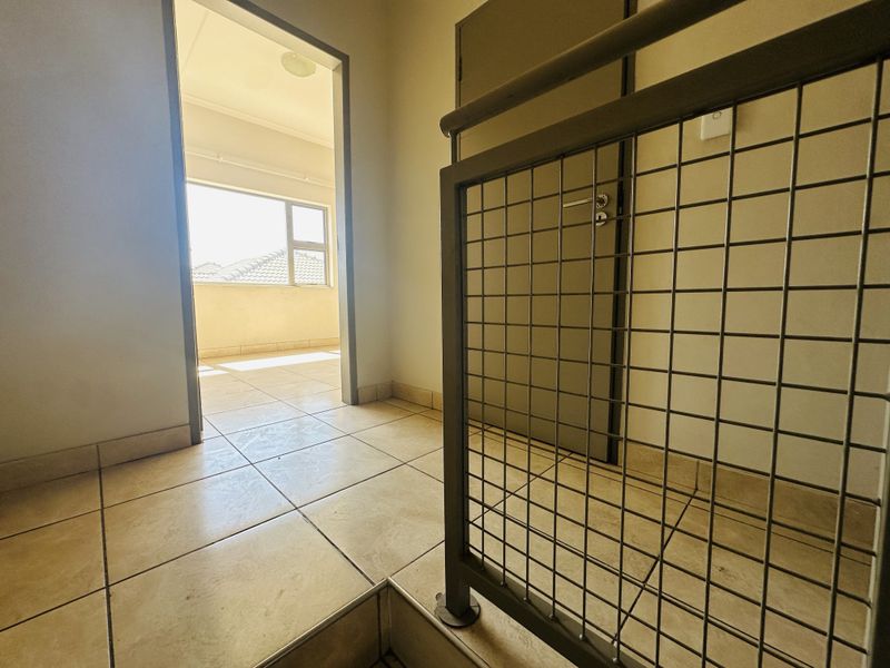 A bright, tiled hallway featuring a metal grid balustrade and access to an adjacent room.