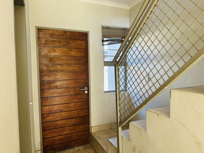 An entry area featuring a timber door, tiled flooring, and a metal staircase railing leading to the upper level.