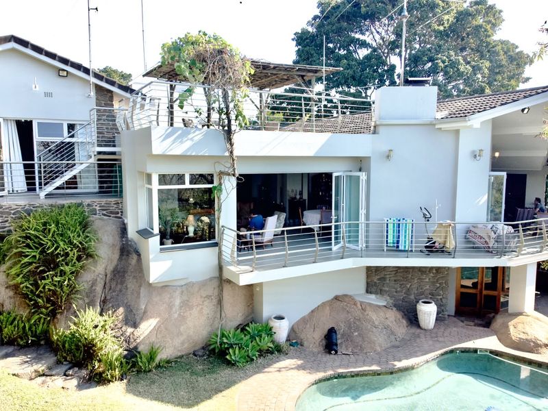 Rear exterior view of a multi-level home featuring a swimming pool, stone-clad walls, and a spacious balcony overlooking the garden.