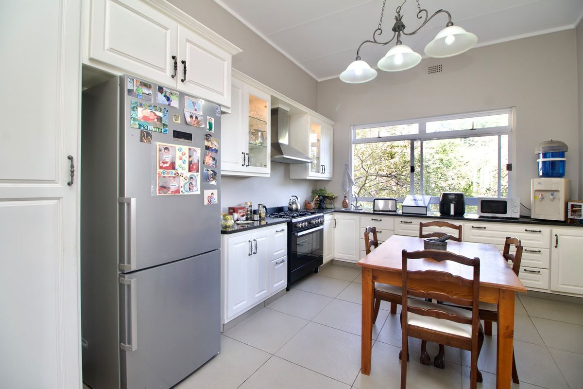 A well-maintained kitchen featuring white shaker-style cabinetry, black granite countertops, a stainless steel gas stove, and tiled flooring with ample natural light.