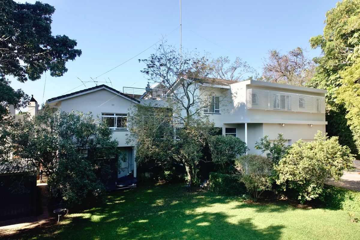 A view of the rear elevation of the house featuring a well-maintained lawn, mature garden, and a mix of traditional and modern architectural elements.