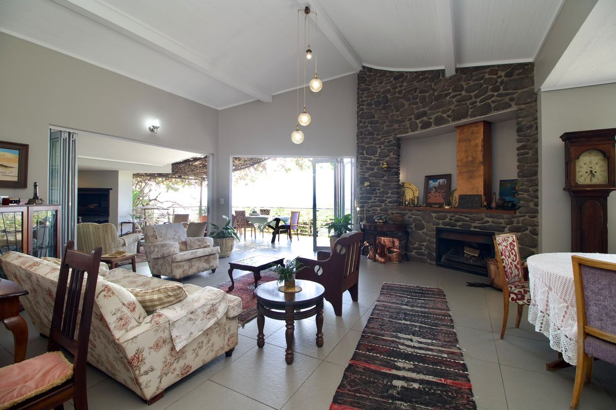Spacious living room featuring a striking stone fireplace with copper chimney, vaulted ceilings with exposed beams, and large bi-fold doors opening to the patio.