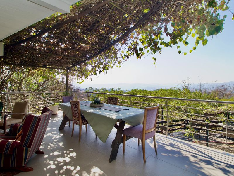 A spacious covered patio featuring a pergola, stainless steel railing, and expansive views of the surrounding landscape.