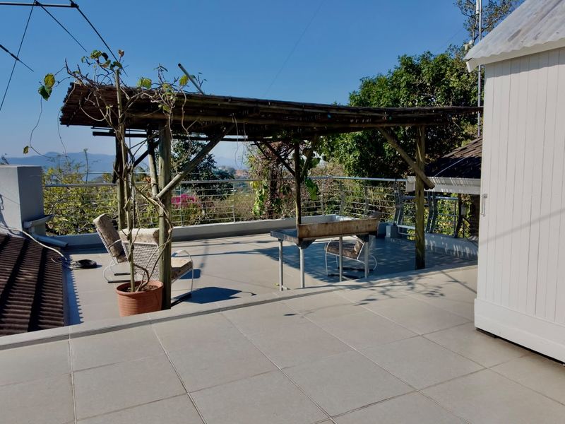 An elevated outdoor patio featuring tiled flooring, a timber pergola, and a built-in braai, offering an open space for outdoor entertainment.