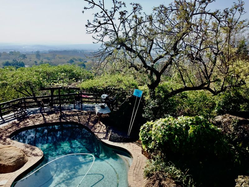 An elevated outdoor pool area featuring a swimming pool with brick paving, surrounded by mature trees and offering expansive landscape views.