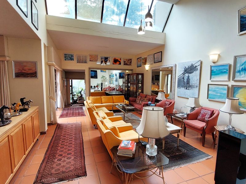 Spacious living room featuring high ceilings with a large skylight, tiled flooring, and built-in cabinetry, offering a bright and airy atmosphere.