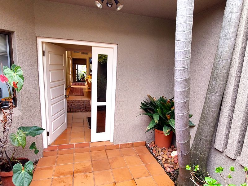 A welcoming entrance area featuring terracotta-style tiled flooring, a panelled front door with a sidelight, and a textured exterior wall finish.