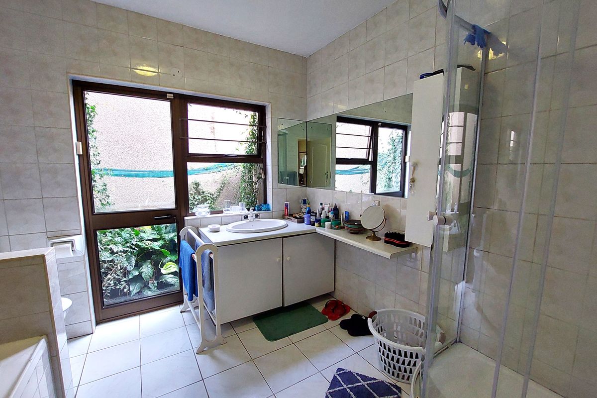 A functional bathroom featuring a vanity with integrated sink, a glass shower enclosure, and floor-to-ceiling wall tiling with direct access to an outdoor area.