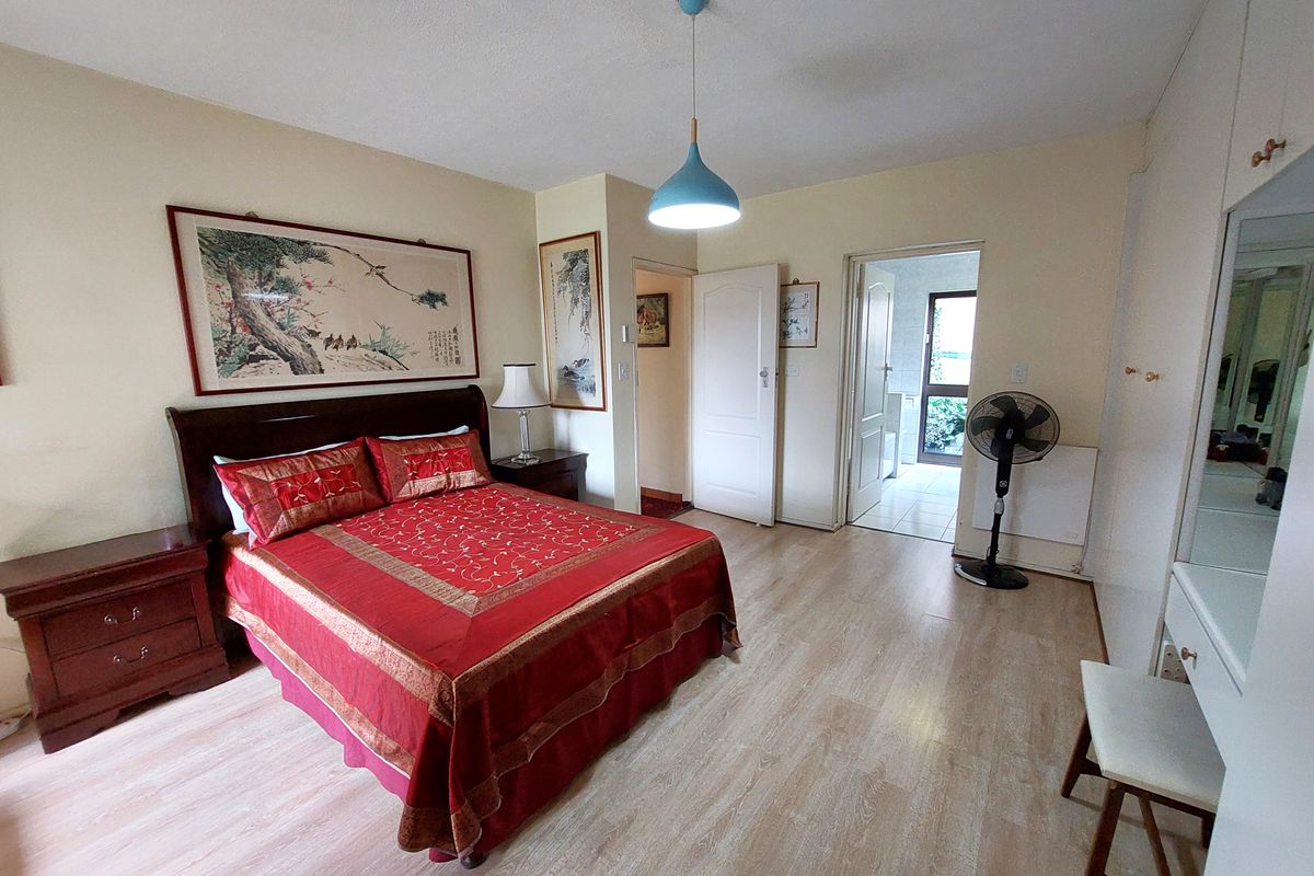 Spacious bedroom featuring light-toned laminate flooring, built-in cupboards, and direct access to an adjoining bathroom area.