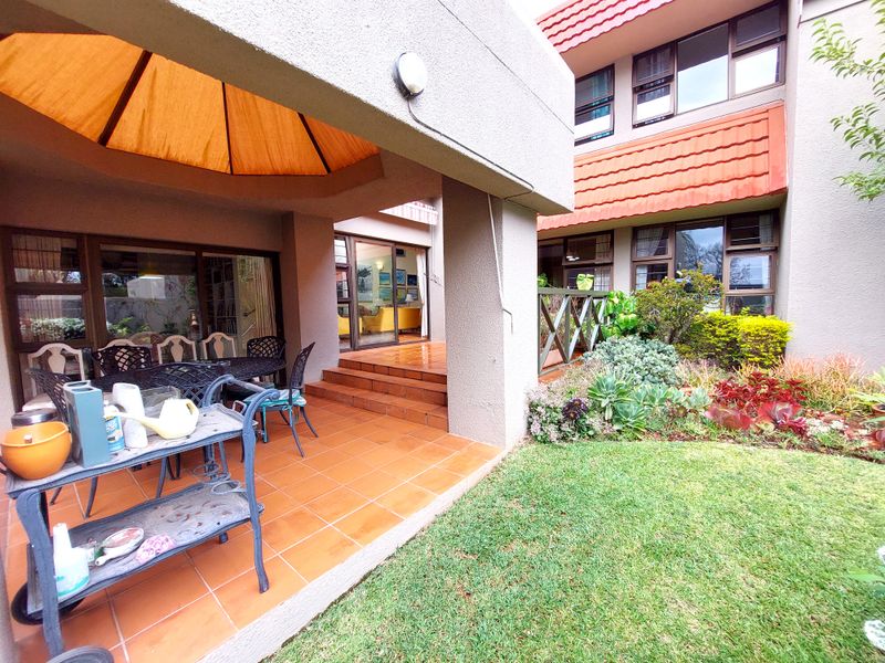A covered patio area with tiled flooring, featuring direct access to the garden and sliding glass doors leading into the townhouse interior.