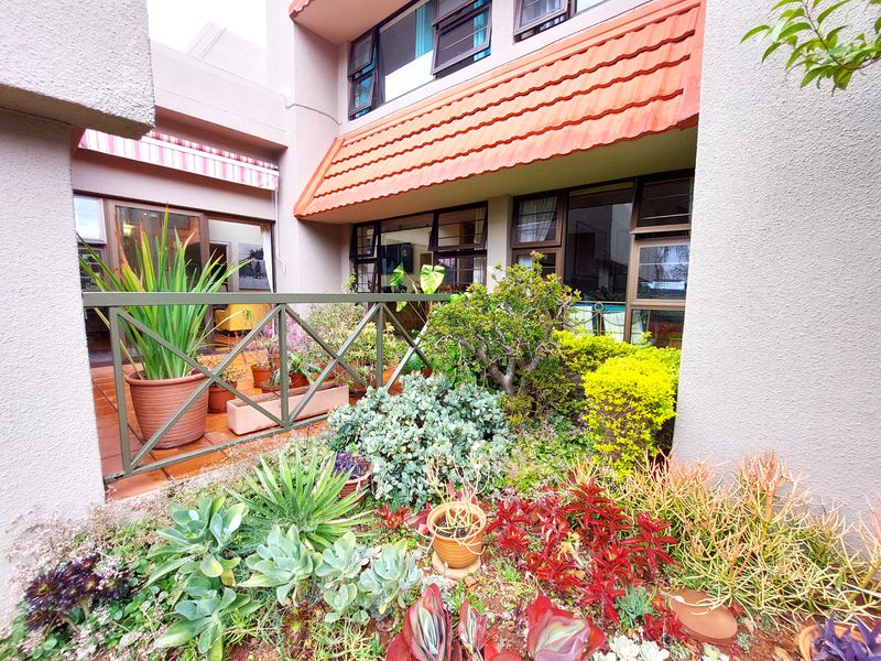 A private patio area featuring terracotta tiling, a metal balustrade, and an integrated awning, overlooking a landscaped garden bed with established shrubs.