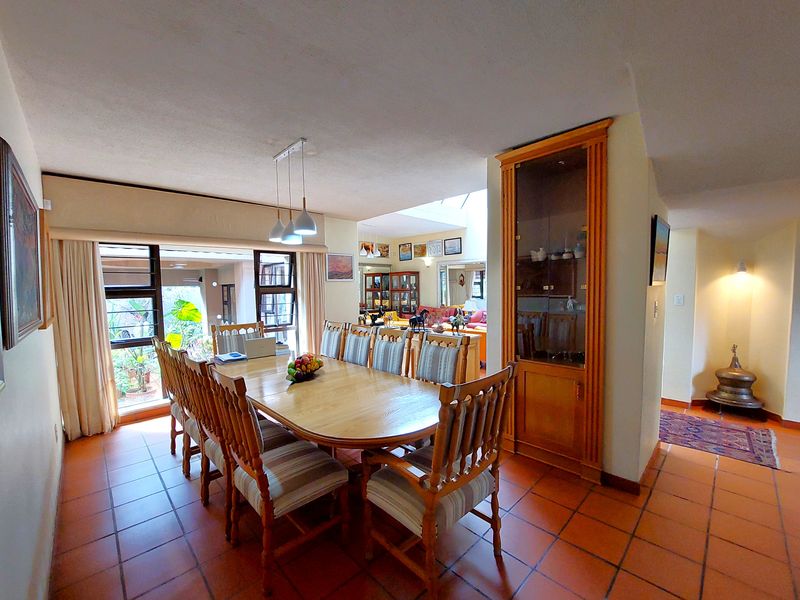 Spacious dining area featuring terracotta floor tiles, a built-in wooden display cabinet, and large windows providing natural light and garden views.