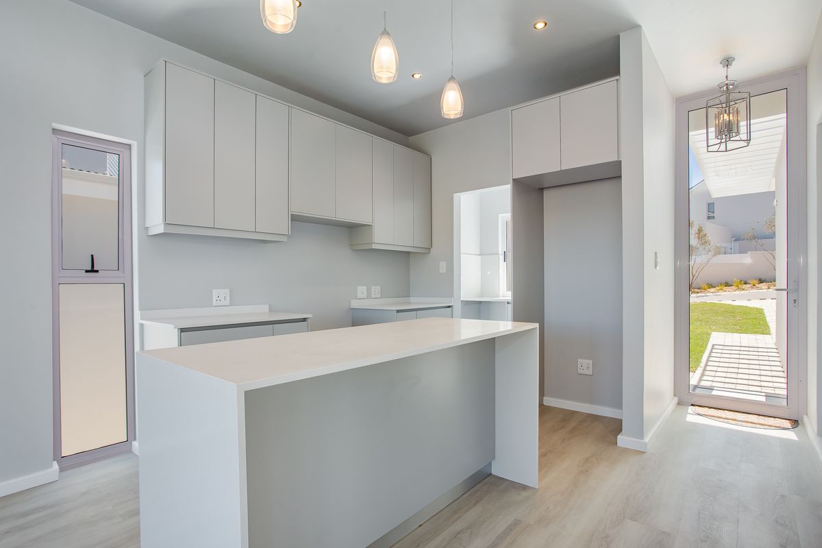 Modern, minimalist kitchen featuring sleek built-in cabinetry, a central island with stone countertops, and direct access to the outdoor area.