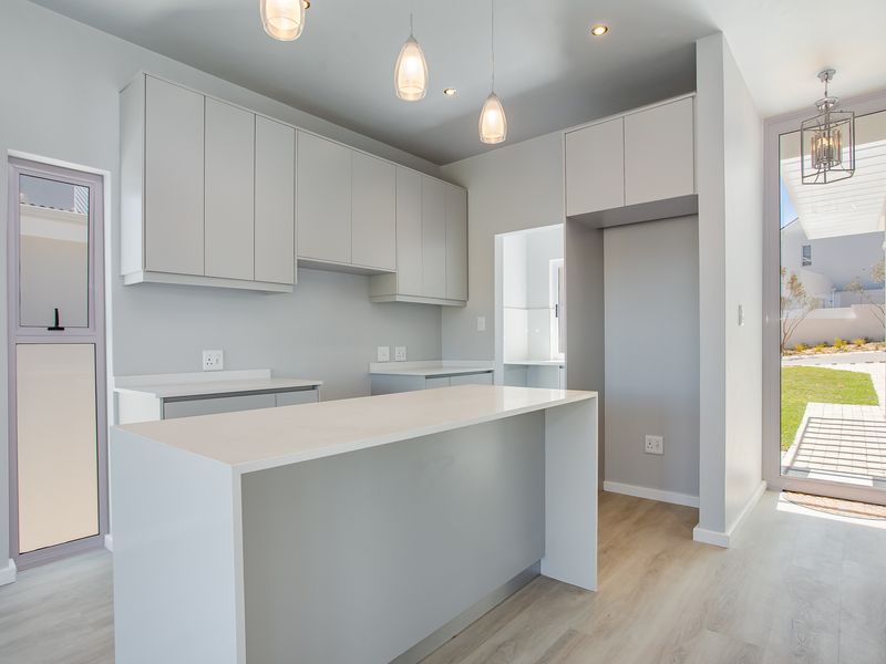 Modern, minimalist kitchen featuring sleek built-in cabinetry, a central island with stone countertops, and direct access to the outdoor area.