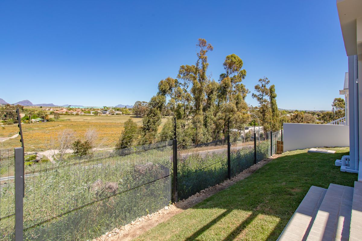 Rear garden area featuring a lawn, concrete steps, and secure mesh fencing with an electric fence overlooking a scenic landscape.