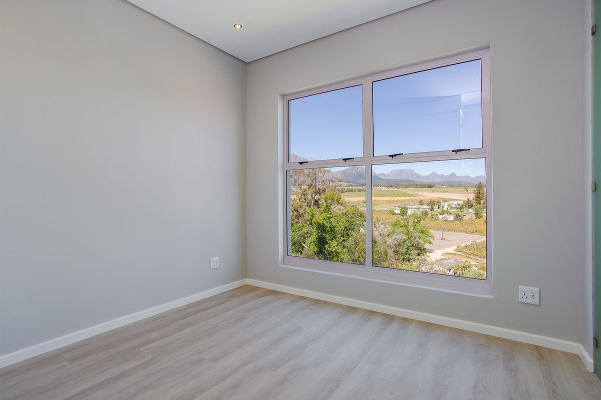 A bright, empty bedroom featuring modern laminate flooring, neutral walls, and a large window offering scenic mountain and landscape views.