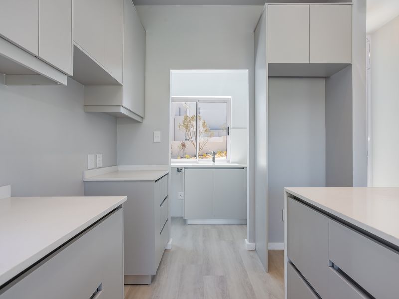 A modern, clean, and empty scullery featuring neutral cabinetry, stone countertops, and a functional sink area with ample storage space.