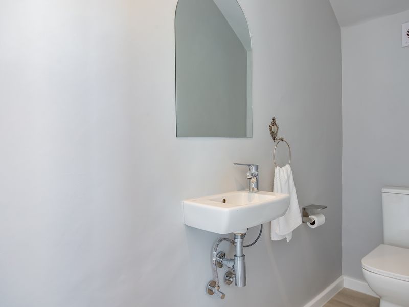 A clean and modern cloakroom bathroom featuring a wall-mounted basin, chrome fixtures, and a toilet.