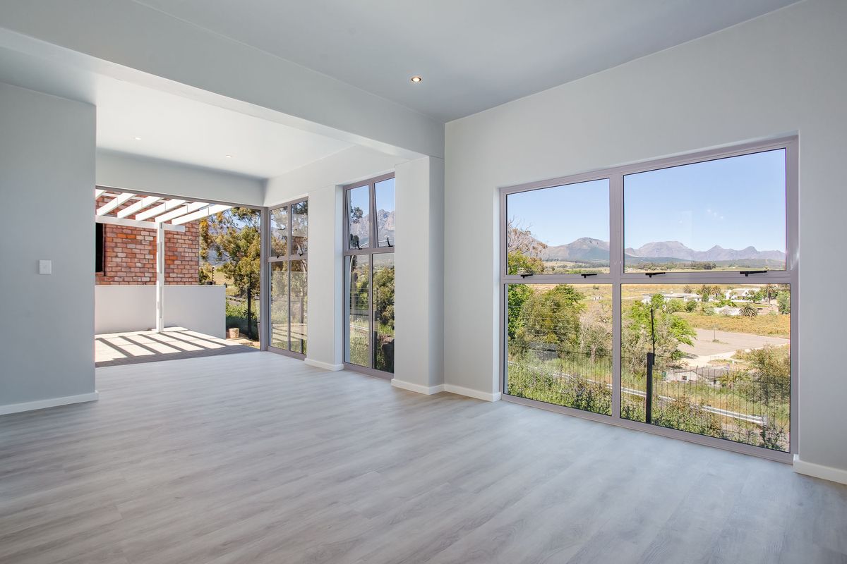 Spacious, light-filled living area featuring modern laminate flooring, large windows with scenic mountain views, and seamless access to a covered outdoor patio.