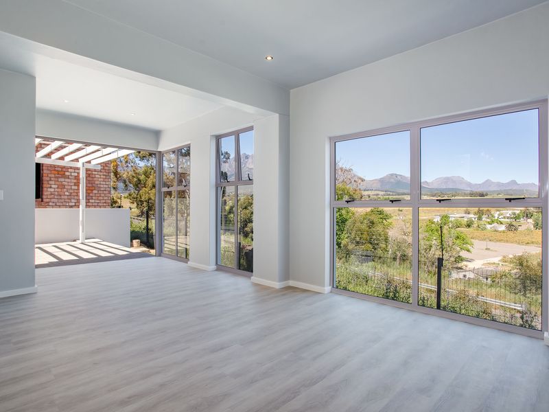 Spacious, light-filled living area featuring modern laminate flooring, large windows with scenic mountain views, and seamless access to a covered outdoor patio.