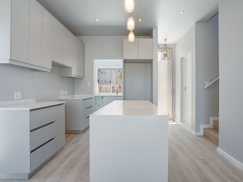 Modern, minimalist kitchen featuring a central island, sleek cabinetry, quartz countertops, and neutral finishes, seamlessly connected to the staircase area.