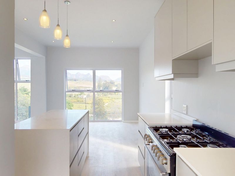 Modern, minimalist kitchen featuring a central island, gas cooktop, built-in oven, and sleek cabinetry with views of the surrounding landscape.