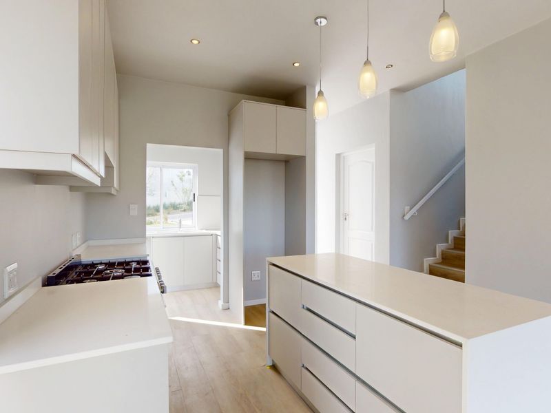 Modern kitchen featuring sleek cabinetry, a central island, gas hob, and integrated lighting, with an adjacent staircase leading to the upper level.