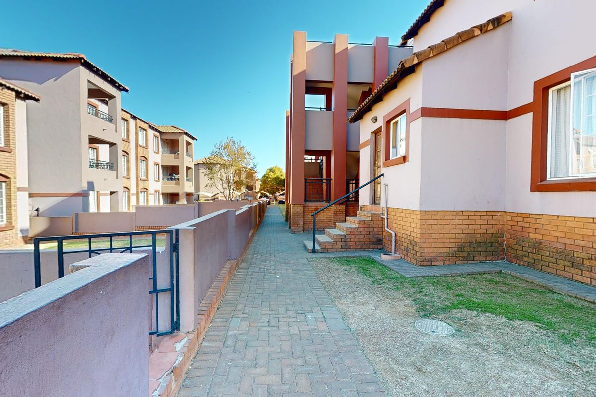 Exterior view of an apartment complex featuring paved walkways, brick boundary walls, and multi-story residential buildings with tiled roofs.