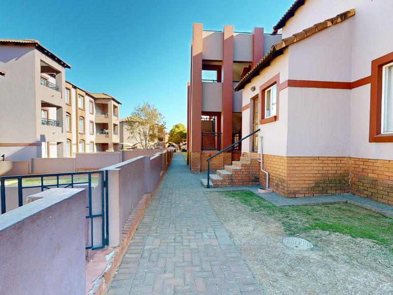 Exterior view of an apartment complex featuring paved walkways, brick boundary walls, and multi-story residential buildings with tiled roofs.