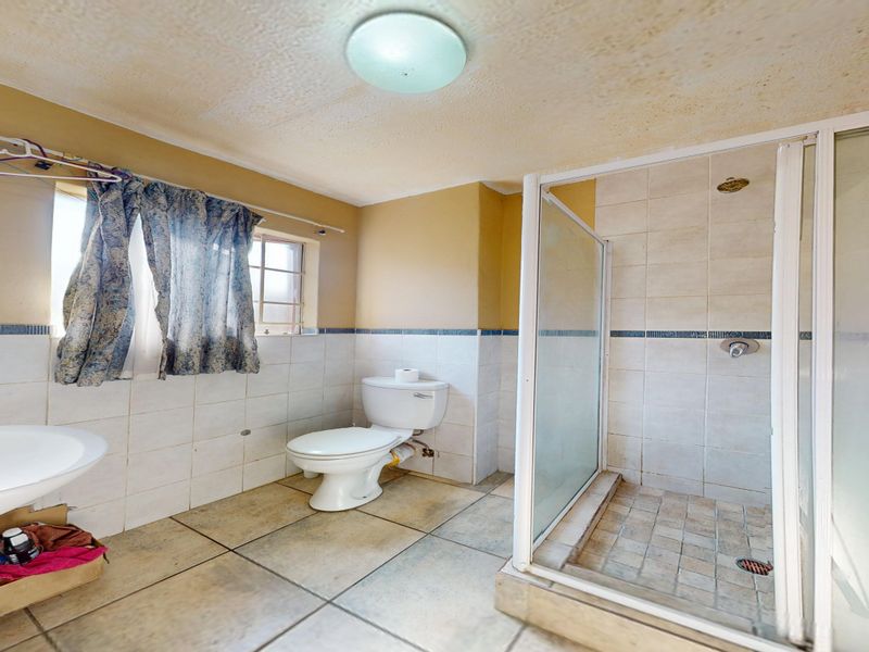 A functional bathroom featuring a shower enclosure, toilet, and pedestal basin with tiled finishes, currently requiring cosmetic updates and ceiling maintenance.