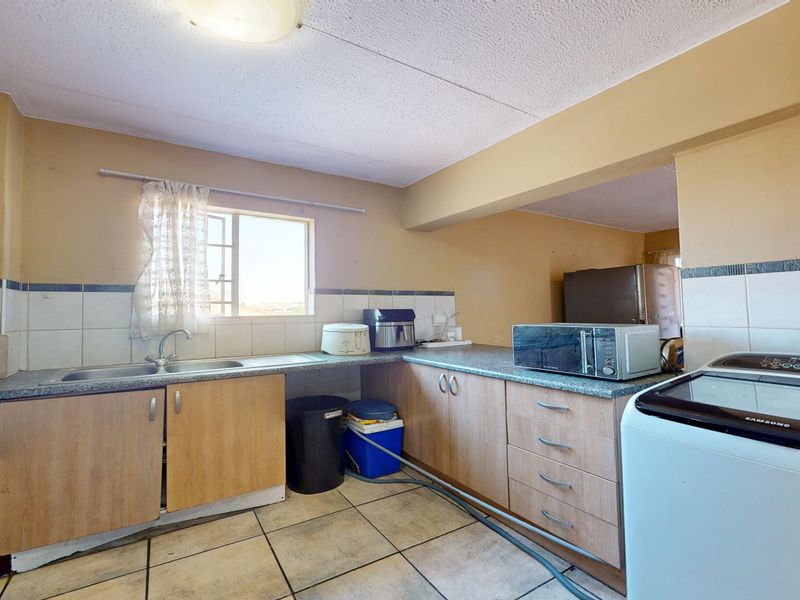 Functional kitchen featuring laminate cabinetry, tiled backsplash, and ceramic flooring, offering a practical layout with potential for modern cosmetic updates.