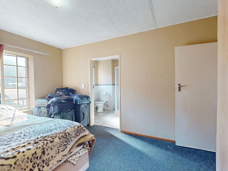 A bedroom featuring a built-in wardrobe, carpeted flooring, and direct access to an en-suite bathroom with a grid-pattern window.