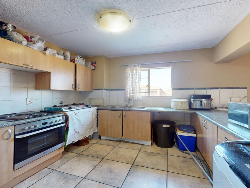 A functional kitchen featuring laminate cabinetry, granite countertops, built-in oven, and hob, with tiled flooring and backsplash throughout.