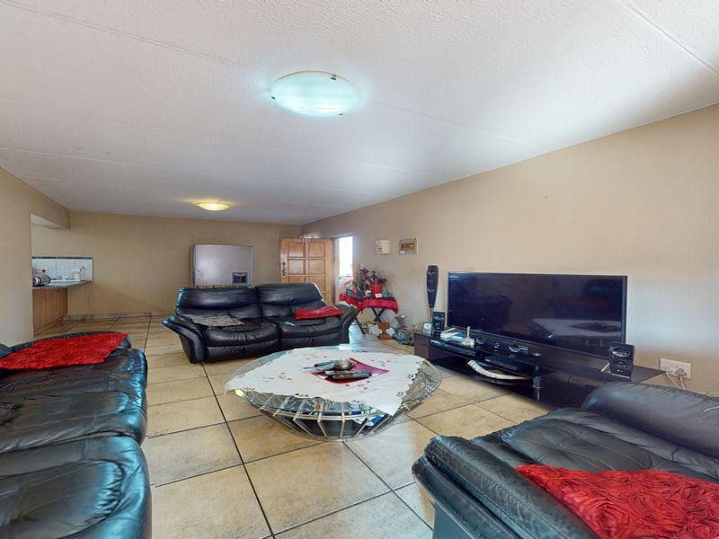 Spacious open-plan living area featuring tiled flooring and integrated kitchen space, offering a functional layout with neutral wall tones.