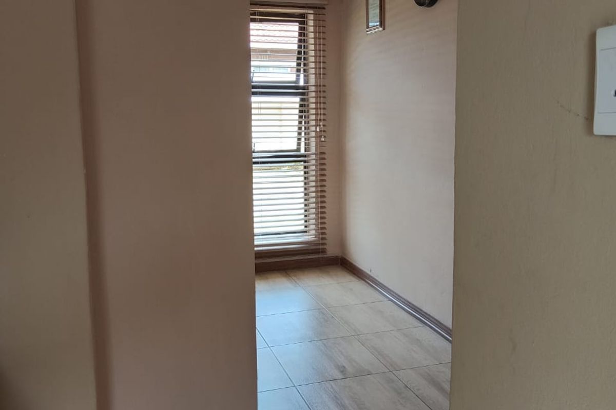 A clean, empty hallway featuring tiled flooring, textured ceiling, and a window fitted with venetian blinds.