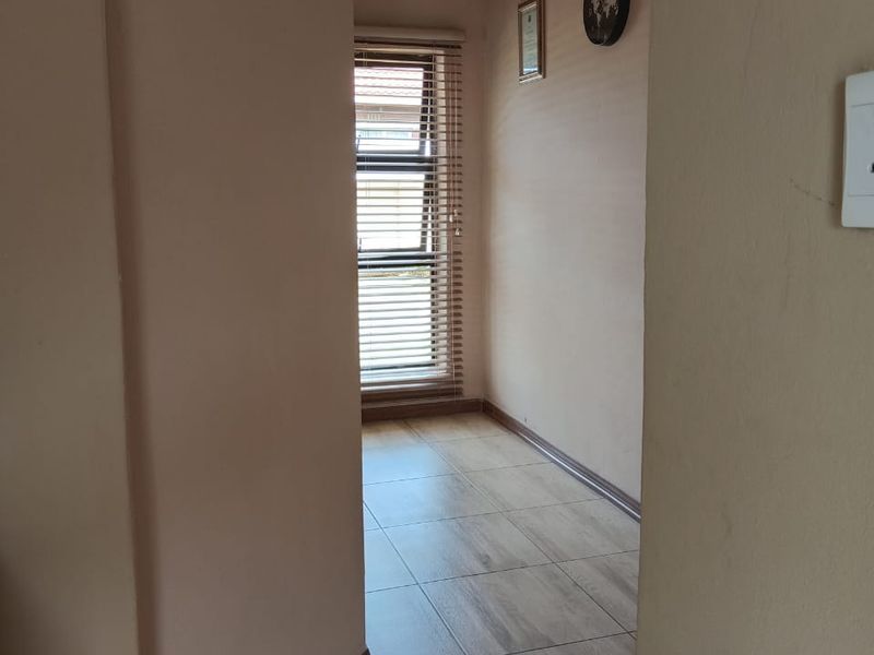 A clean, empty hallway featuring tiled flooring, textured ceiling, and a window fitted with venetian blinds.