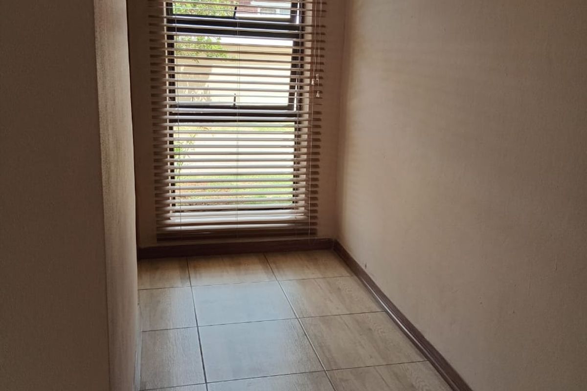 A clean, empty hallway featuring neutral tiled flooring, coved ceiling details, and a window fitted with venetian blinds.
