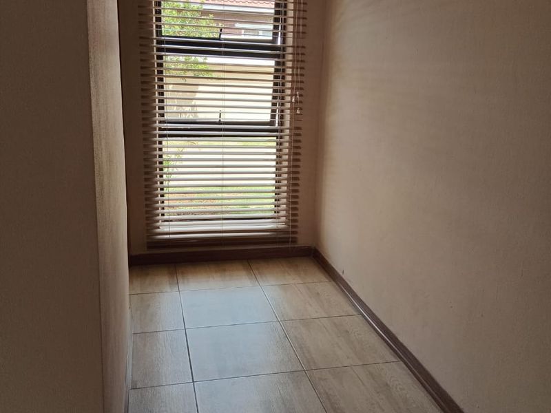 A clean, empty hallway featuring neutral tiled flooring, coved ceiling details, and a window fitted with venetian blinds.