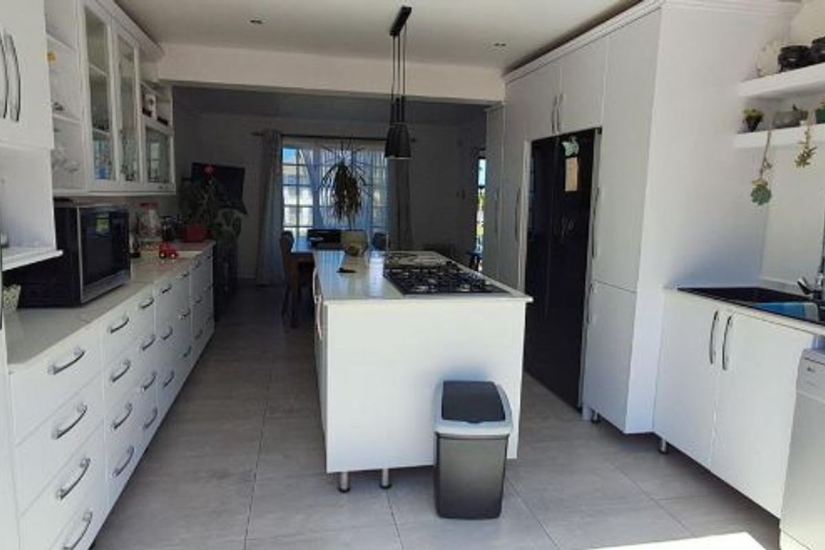 Modern kitchen featuring a central island with a gas hob, extensive white cabinetry, tiled flooring, and integrated sink fixtures.