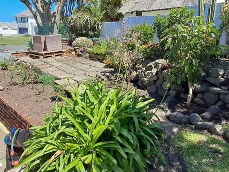 A tiered garden area featuring a stone retaining wall, paved patio section, and established garden beds with mature plantings.