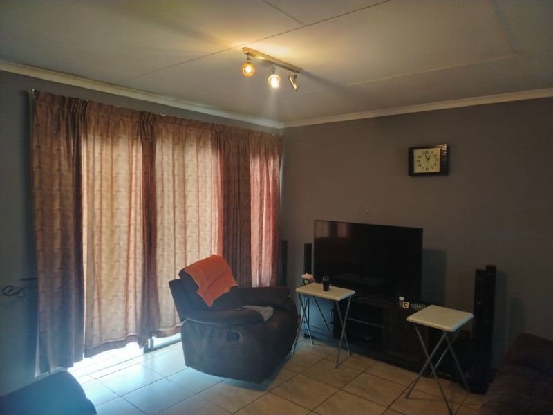 A living room featuring tiled flooring, a sliding glass door with curtains, and overhead track lighting.