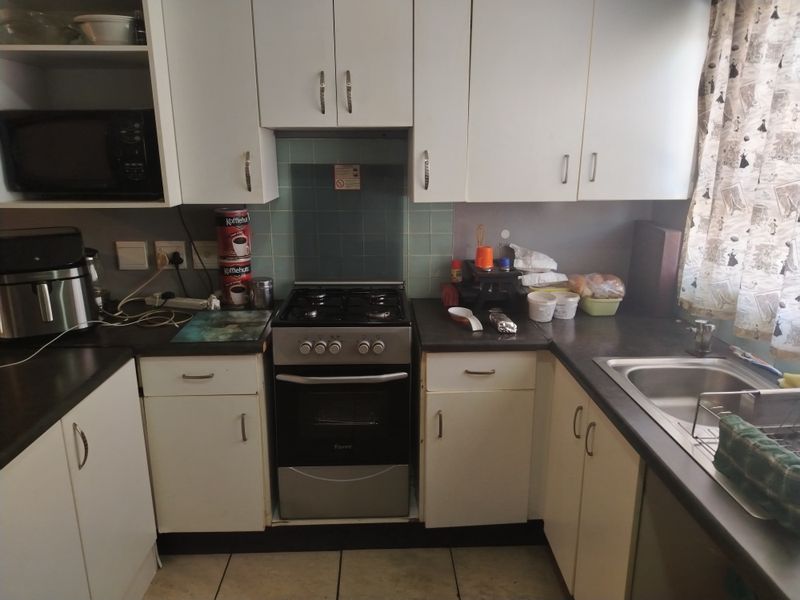 Compact kitchen featuring white cabinetry, a gas stove with oven, dark laminate countertops, and a stainless steel sink.