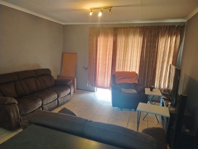 A living room featuring tiled flooring, ceiling-mounted track lighting, and a sliding glass door providing access to the exterior.