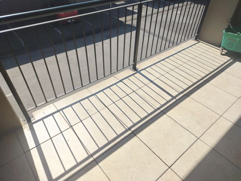 A simple balcony area featuring tiled flooring and a metal balustrade overlooking the parking area.