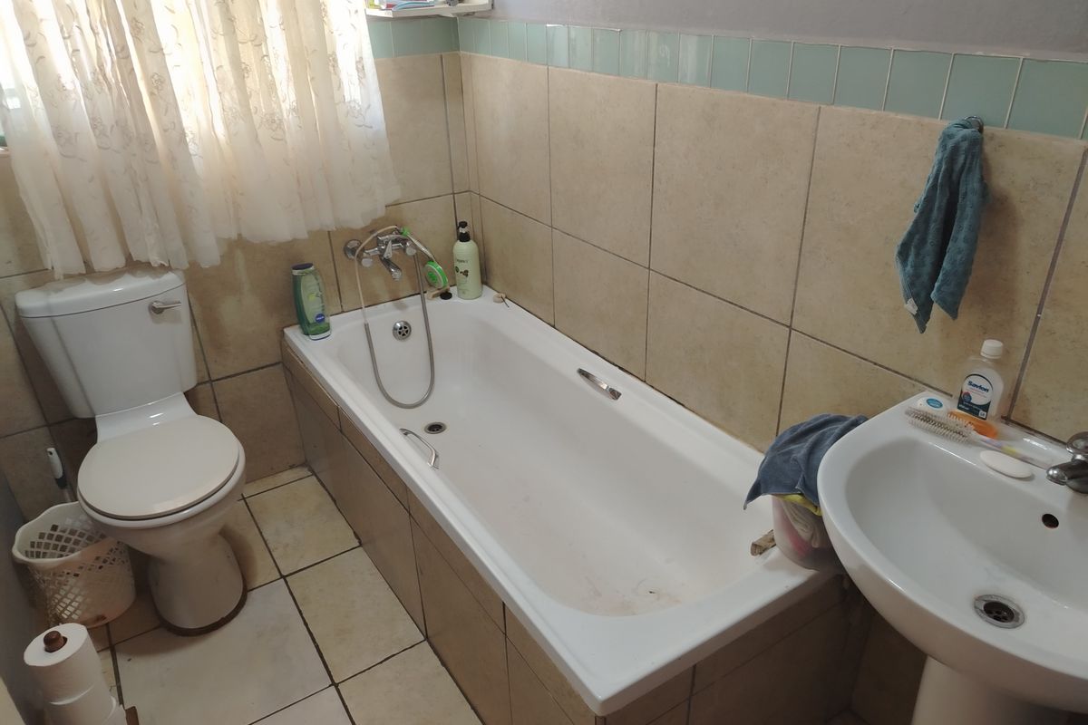 A functional bathroom featuring a standard bathtub, pedestal basin, and toilet with neutral wall and floor tiling.