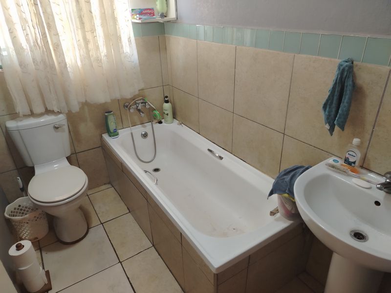 A functional bathroom featuring a standard bathtub, pedestal basin, and toilet with neutral wall and floor tiling.
