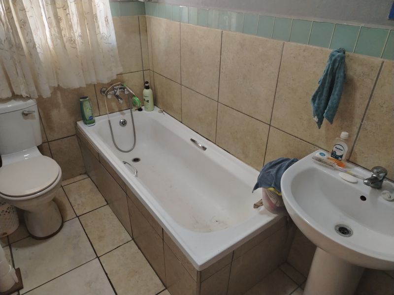 A dated bathroom featuring a standard bathtub, pedestal basin, and toilet with neutral wall and floor tiling.
