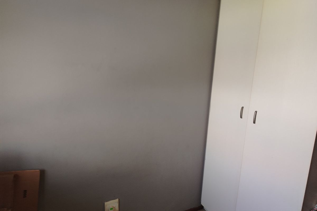 A bedroom interior featuring a neutral grey wall and a white built-in wardrobe with modern handles.